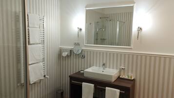 Un bagno con doccia, lavandino, specchio e carta da parati a righe.