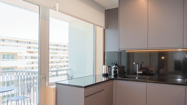 A modern kitchen with grey cabinets, a black countertop, and a window overlooking a balcony. - Allegro Boutique Apartment B (Porto)