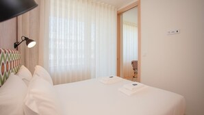 A neatly made bed with white linens, a lamp on the left, and sheer curtains covering the window. - Allegro Boutique Apartment B (Porto)