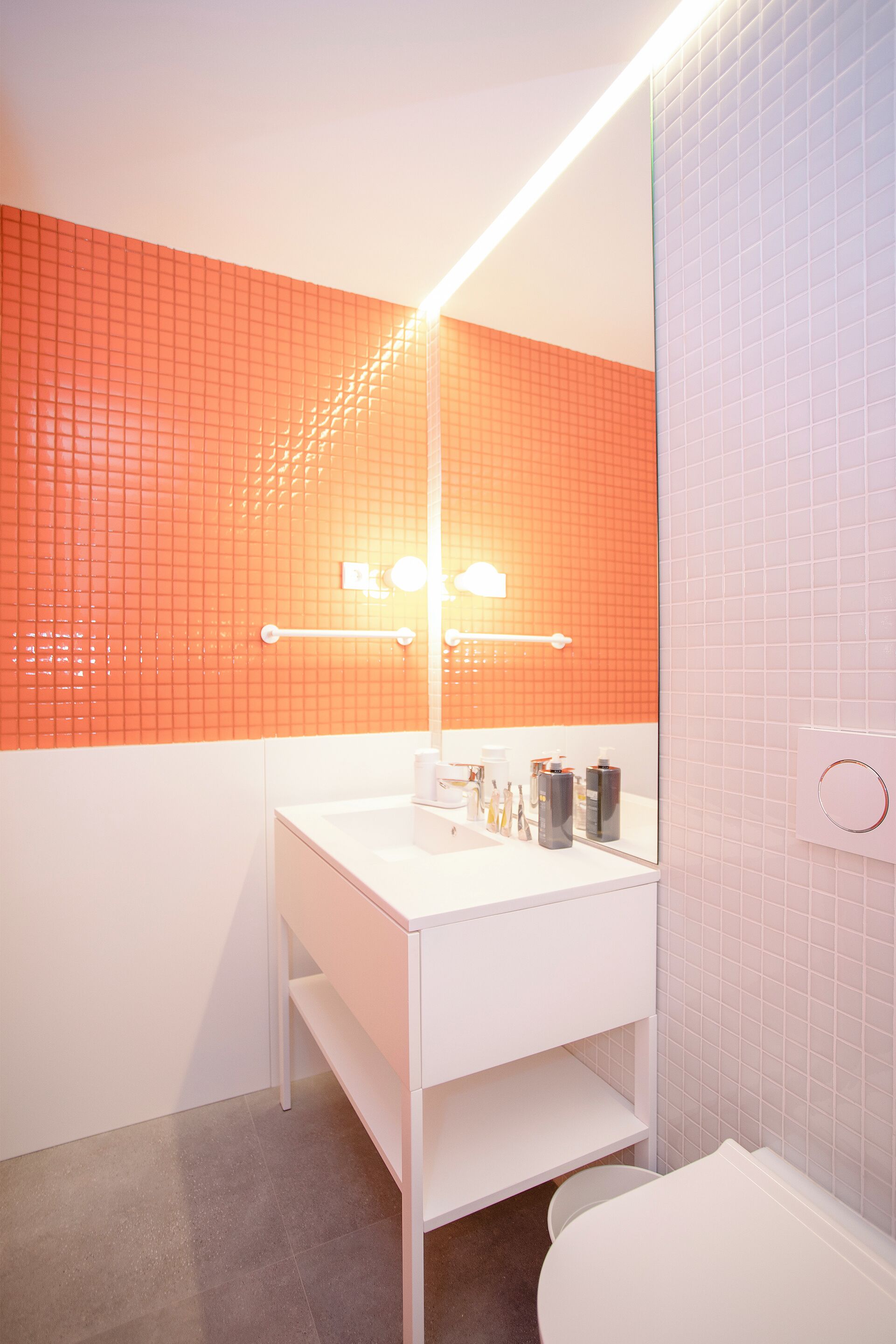 A bathroom with a white sink, orange tiled wall, and a white toilet.