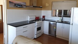 Een compacte keuken met witte kastjes, een gasfornuis, een vaatwasser en een koelkast.