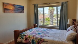 Een slaapkamer met een bed, een raam met gordijnen, een schilderij aan de muur en uitzicht op buiten.