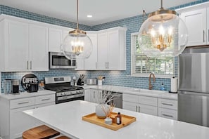 Una cocina moderna con armarios blancos, una isla central, una zona de café e iluminación colgante.