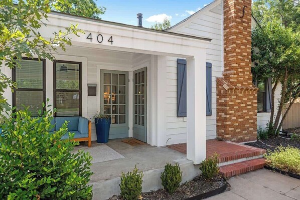 Una casa con el número '404' en la fachada, una chimenea de ladrillo, una puerta azul y un banco azul en el exterior.