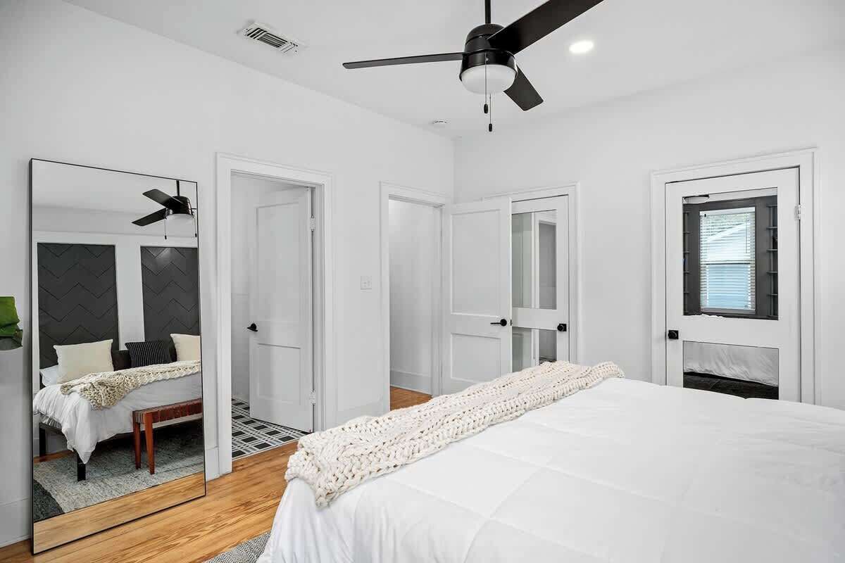 A bedroom with a bed, a ceiling fan, a mirror, and a door.