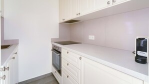 Una cocina con armarios blancos, horno empotrado y una cafetera Krups sobre la encimera.