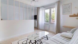 Una sala moderna con un sofá, una mesita de centro y un televisor. Hay un ventanal corredero que da a un área exterior.