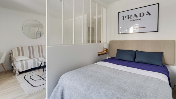 Un dormitorio moderno con cama, sofá, espejo y un cartel enmarcado en la pared.