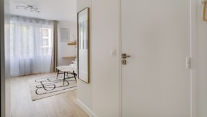 Una habitación con una puerta blanca, una silla blanca, un espejo y un tapete de color claro.