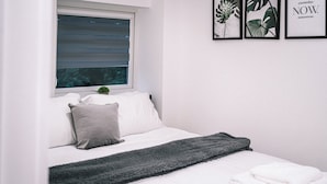 A neatly made bed with a grey blanket, white pillows, and a small plant on the windowsill. - Stunning 2-bed Apartment in Banbury (Banbury)