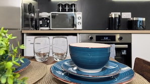 A modern kitchen with stainless steel appliances, including a microwave and coffee maker, and a dining area with blue plates and glasses. - Stunning 2-bed Apartment in Banbury (Banbury)