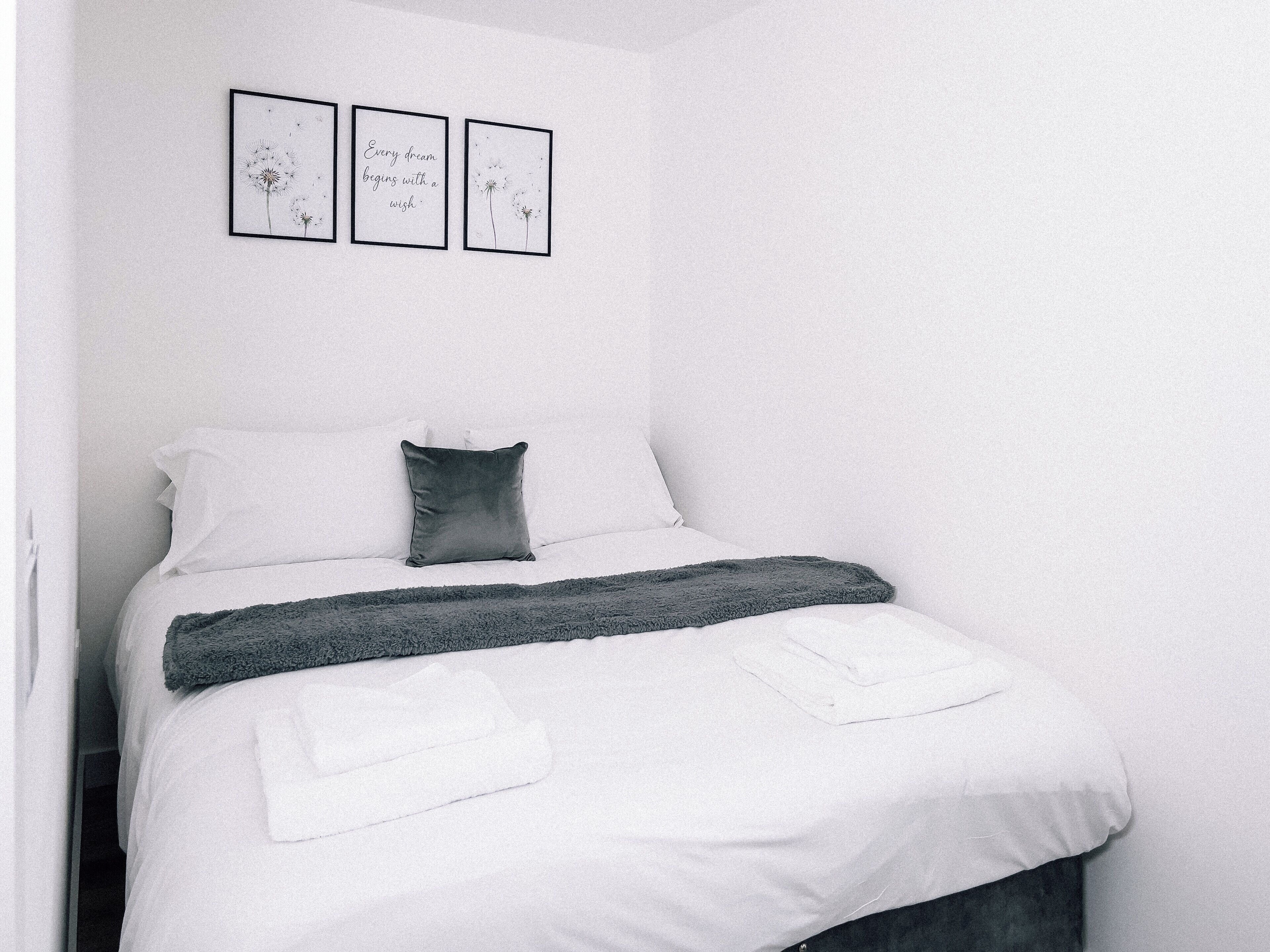 A neatly made bed with white linens, a dark gray throw blanket, and a pillow. Above the bed, there are three framed pictures on the wall.