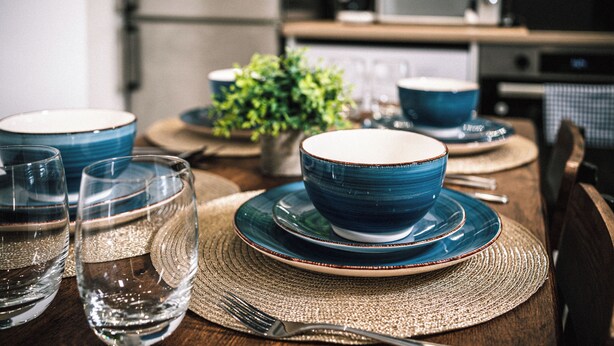 A dining table set with blue bowls, plates, and glasses, with a woven placemat. - Stunning 2-bed Apartment in Banbury (Banbury)