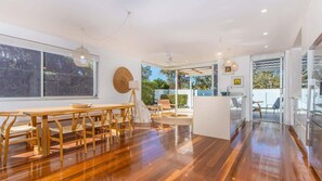 A spacious room with a wooden dining table and chairs, a large window, and a view of the outdoors. - Verano (Casuarina)
