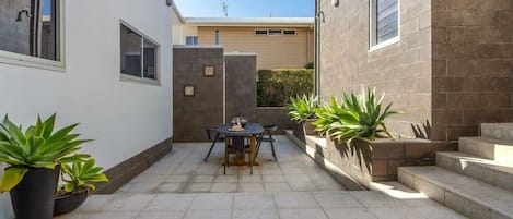 Un patio con mesa y sillas, plantas en macetas y una escalera que sube a un nivel superior.