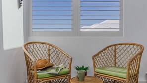 Two wicker chairs with green cushions and a woven basket, positioned in front of a window with horizontal blinds.