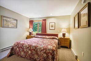 A bedroom with a large bed, two bedside tables, a window with curtains, and framed pictures on the walls. - Settle Into Something Special D14 (Killington)