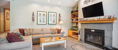 A living room with a sofa, coffee table, fireplace, TV, and framed pictures on the wall.