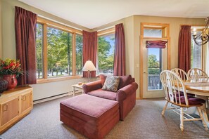 A cozy room with a large window, a sofa, a table with chairs, and a cabinet.