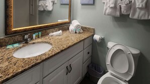 Un baño con lavamanos de encimera de granito, un espejo grande, inodoro y toallas colgadas en la pared.