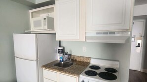 Una cocina compacta con armarios blancos, un microondas, una estufa y un refrigerador.