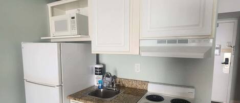 A compact kitchen with white cabinets, a microwave, a stove, and a refrigerator.