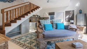 A spacious living area with a wooden staircase, a sofa with patterned cushions, a coffee table, and a kitchen in the background. - One bedroom private pool romantic villa (Bali)