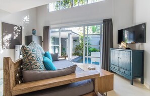 A modern living room with a sofa, a wooden coffee table, a TV, and a view of a pool and garden through large glass doors. - One bedroom private pool romantic villa (Bali)