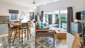A spacious living area with a dining table, sofa, and TV. There is a balcony with plants and a view of the outdoors. - One bedroom private pool romantic villa (Bali)