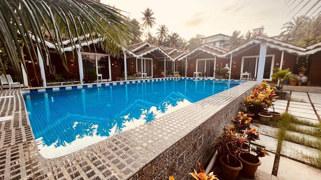 A swimming pool with a tiled edge, surrounded by potted plants and a covered seating area with a tiled roof.