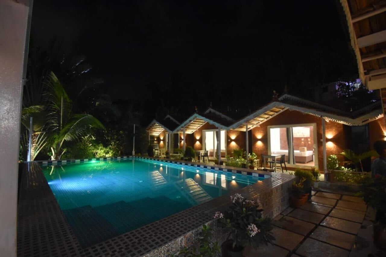 A nighttime view of a hotel with a swimming pool, well-lit rooms, and a tropical garden.