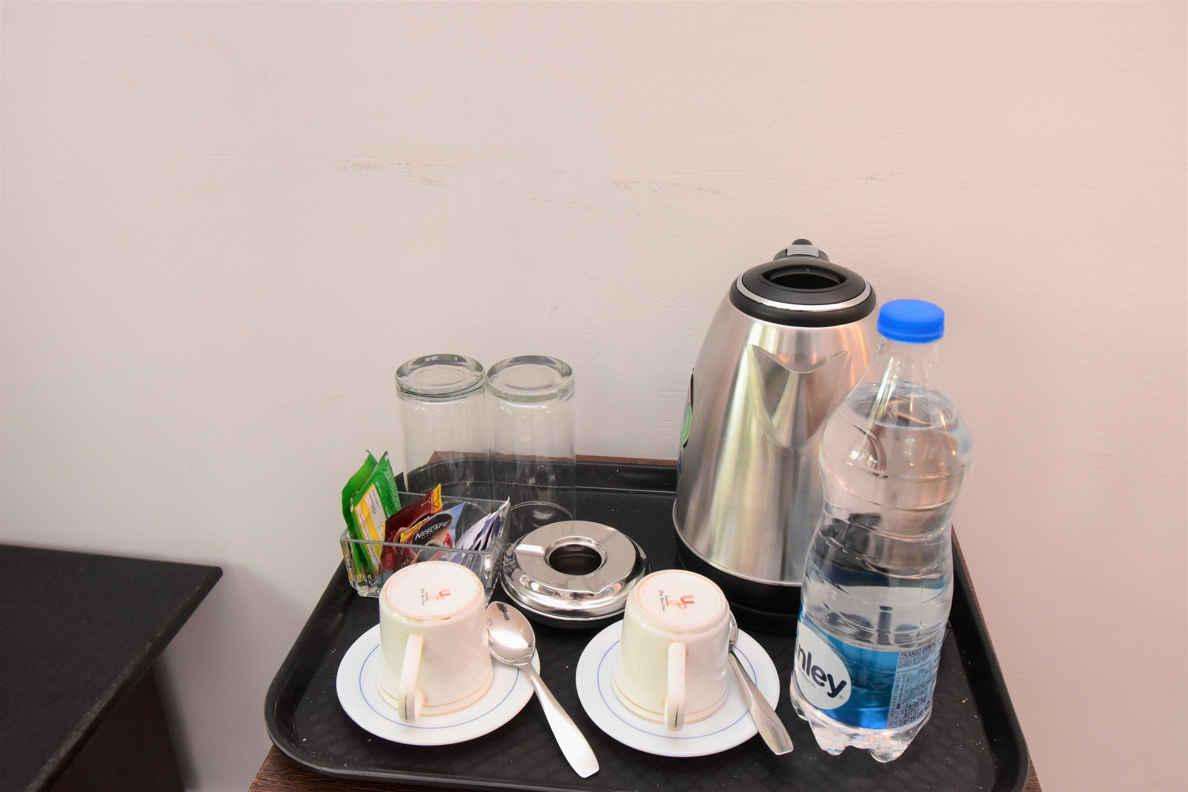 A tray with two cups, a spoon, a bottle of water, and a thermos on a black tray.