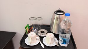 Een dienblad met twee bekers, een lepel, een fles water en een thermosfles op een zwart dienblad.