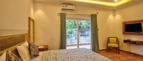 A bedroom with a bed, a ceiling fan, an air conditioning unit, a TV mounted on the wall, and a view of the outdoors through a sliding door.