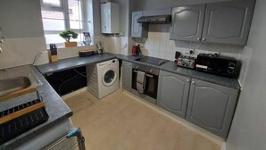 A compact kitchen with grey cabinets, a washing machine, a dishwasher, a toaster, and a microwave. - Charming Three Bedroom 5 Double Bed Apt in London (London)