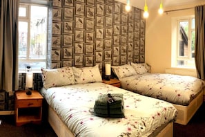 A bedroom with two beds, a wall of framed bird illustrations, a bedside table with a lamp, and a window with curtains. - Charming Three Bedroom 5 Double Bed Apt in London (London)