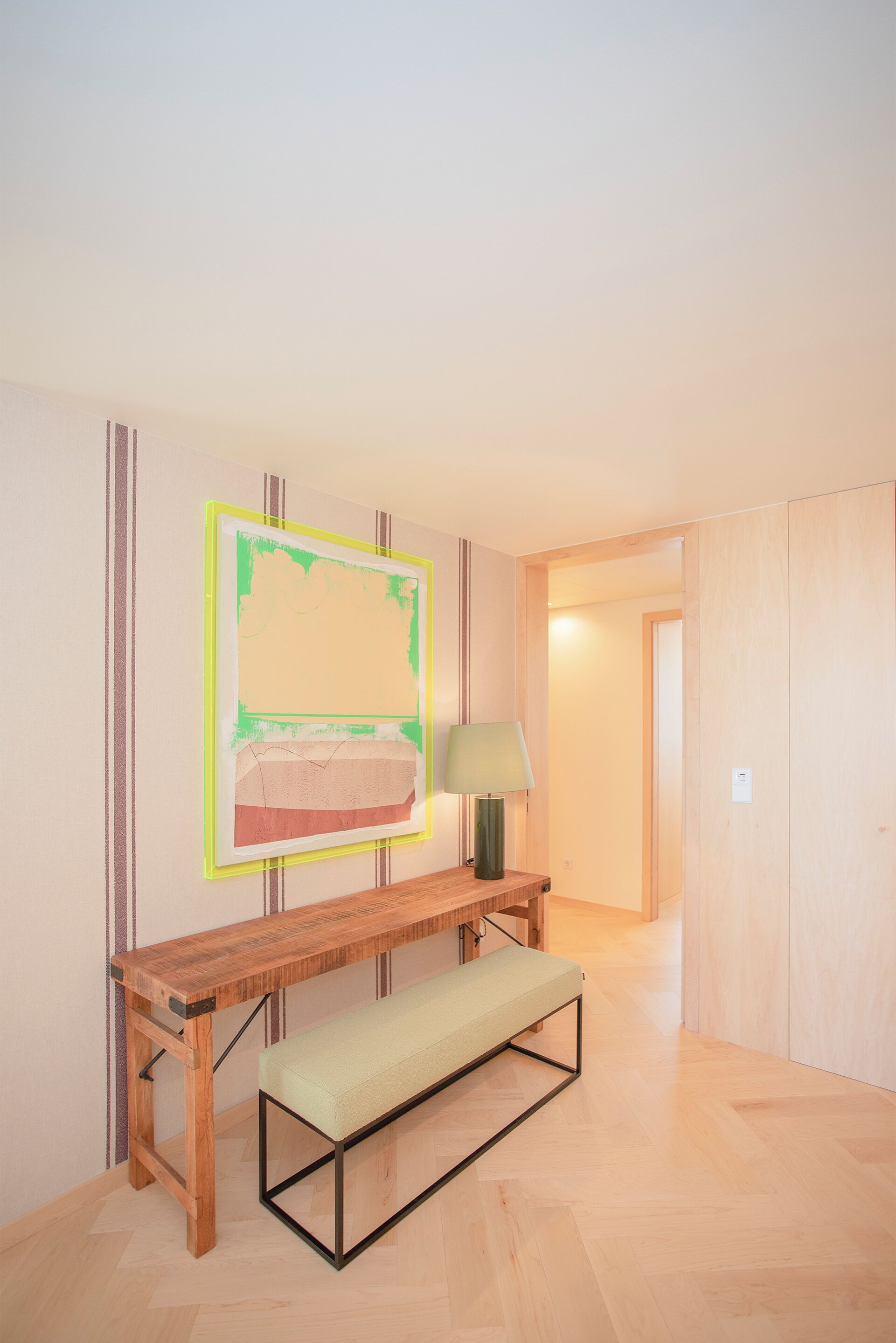 A room with a wooden bench, a table, and a wall-mounted artwork.