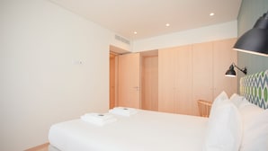 A modern hotel room with a neatly made bed, a bedside lamp, and a wooden wardrobe.