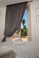Un dormitorio con una cama, una ventana con cortinas y vistas a palmeras afuera.