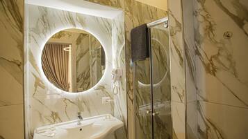 Un baño con lavamanos de mármol, un espejo con marco circular y una cabina de ducha de vidrio.