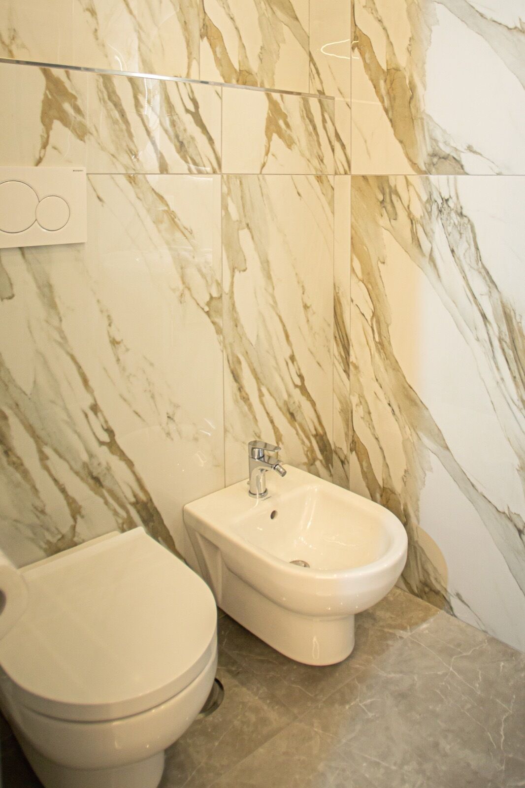 Une salle de bain avec un mur en marbre, un bidet et des toilettes.