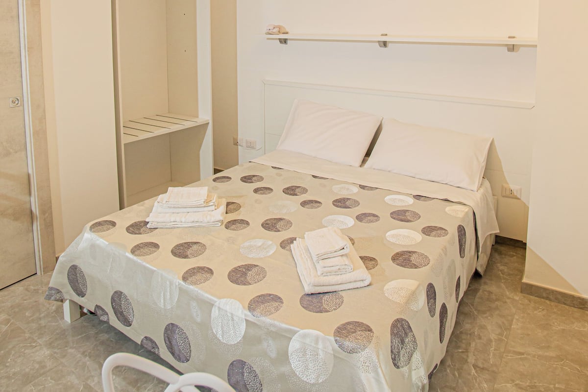 Un dormitorio moderno con cama, mesita de noche, espejo y lámpara circular.