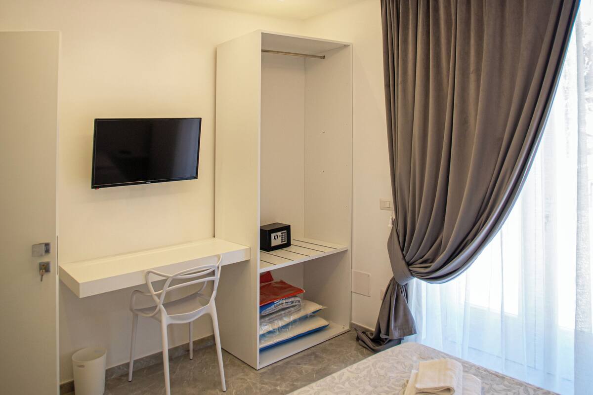 Una habitación de hotel moderna con una cama, un escritorio, una silla, un televisor y un armario.