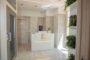 Zona de recepción con un mostrador de mármol, una planta en maceta y una puerta de cristal.