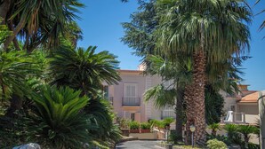 A cobblestone street lined with palm trees and potted plants, leading to a building with balconies and a tiled roof. - Forever luxury rooms (Castellammare di Stabia)