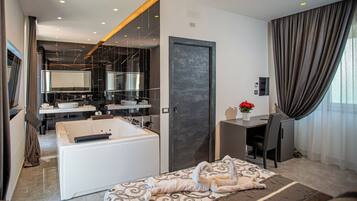 A modern hotel room with a separate living area, a large mirror, a bathtub, and a desk with a chair.