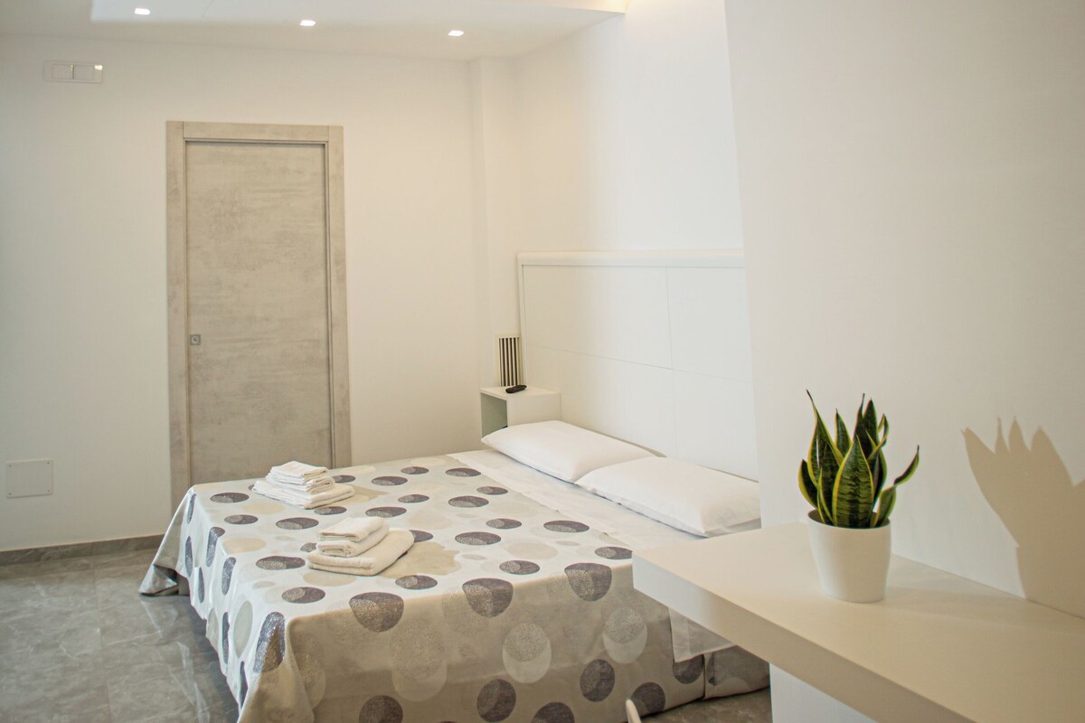 A modern bedroom with a bed, a bedside table, a chair, and a potted plant.