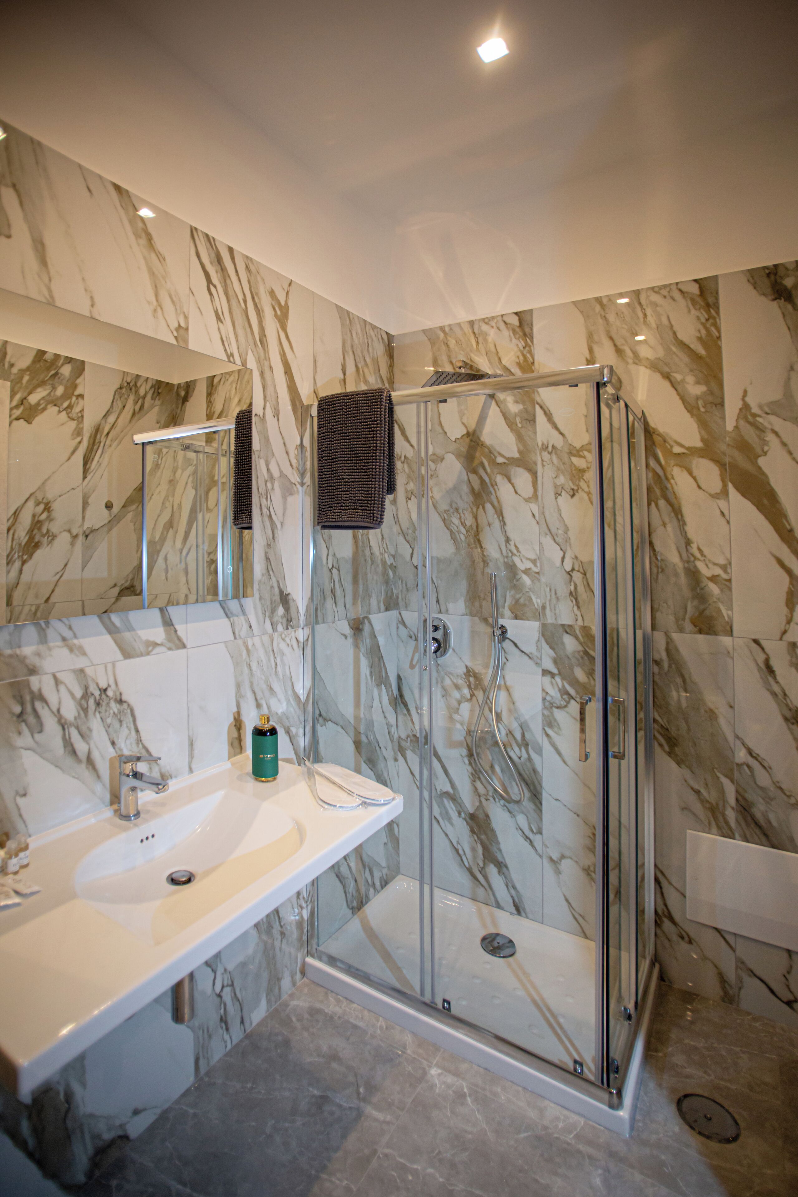 Un bagno moderno con una parete in marmo, un box doccia in vetro e un lavandino bianco.