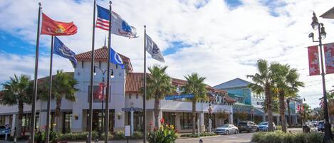A commercial area with multiple flags, palm trees, and a paved street.