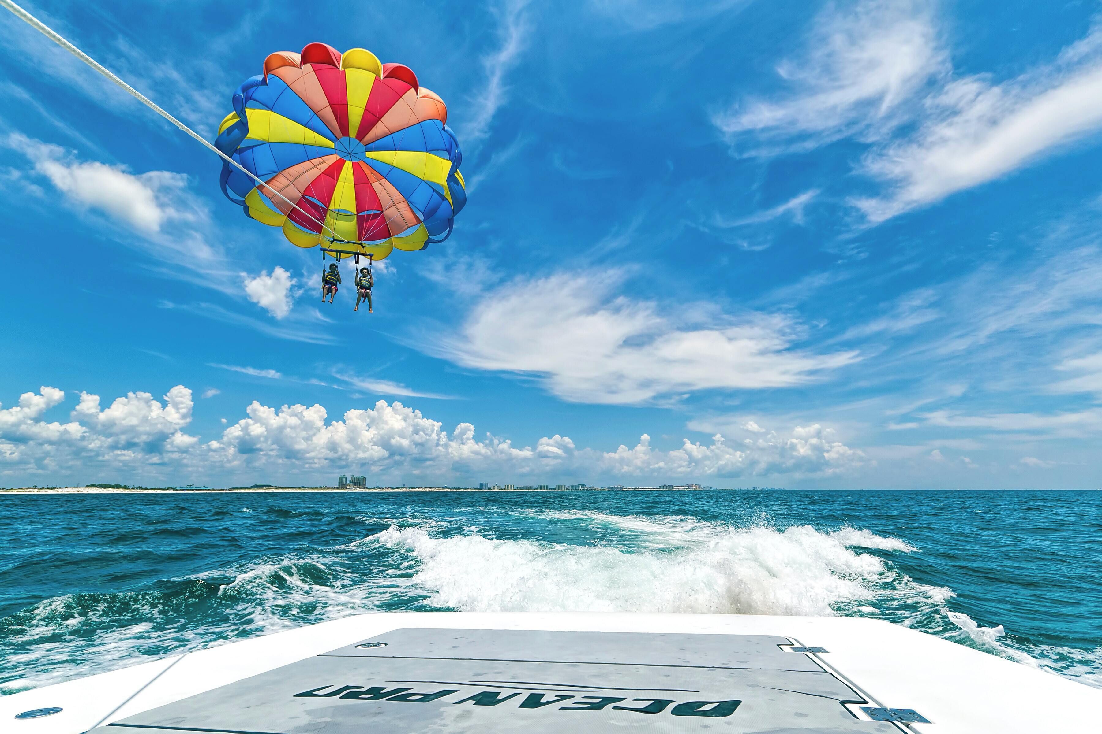 Een parasail met meerdere personen, een boot en een helderblauwe lucht boven de oceaan.